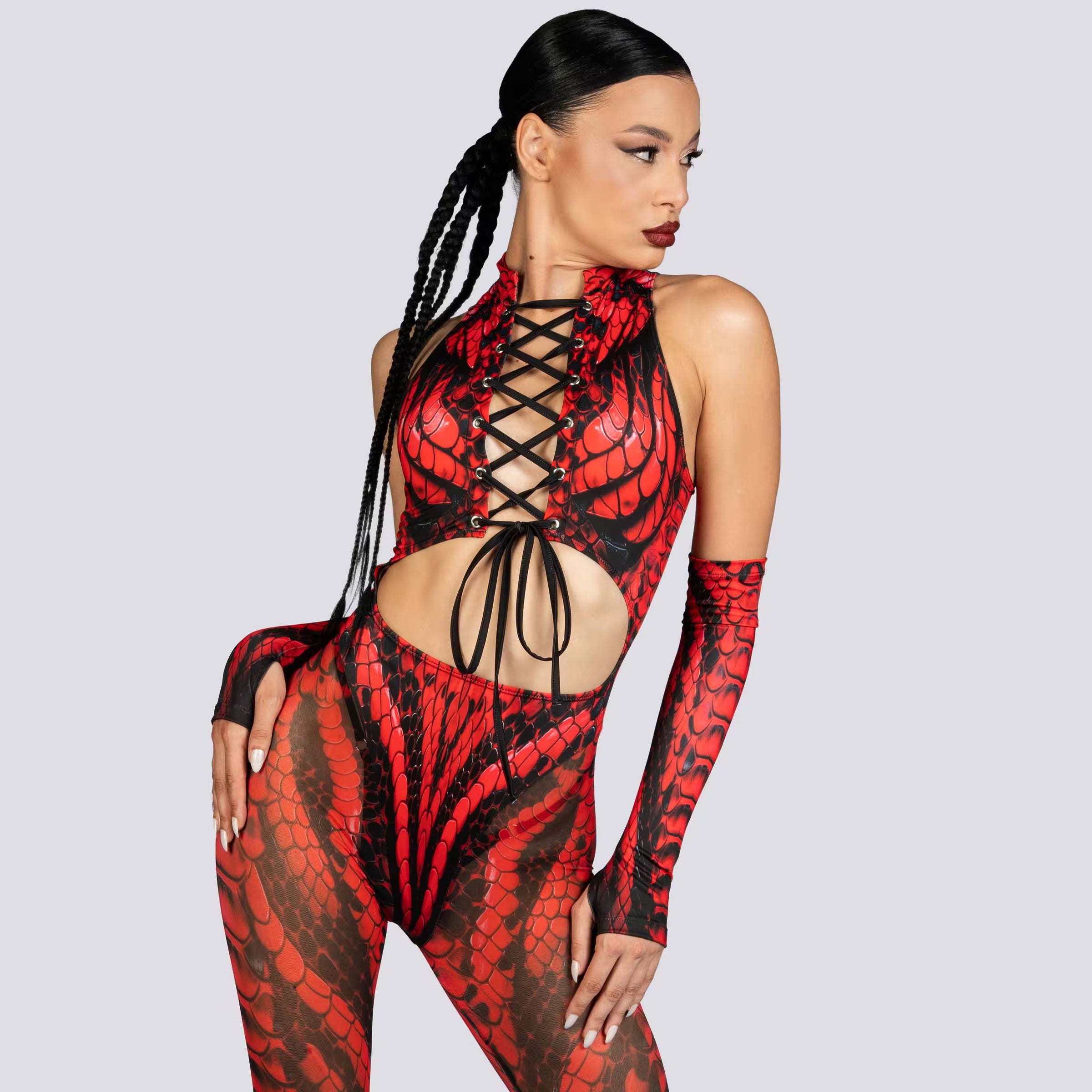 Woman wearing a red and black reptile-print cutout bodysuit with matching arm sleeves and black combat boots.