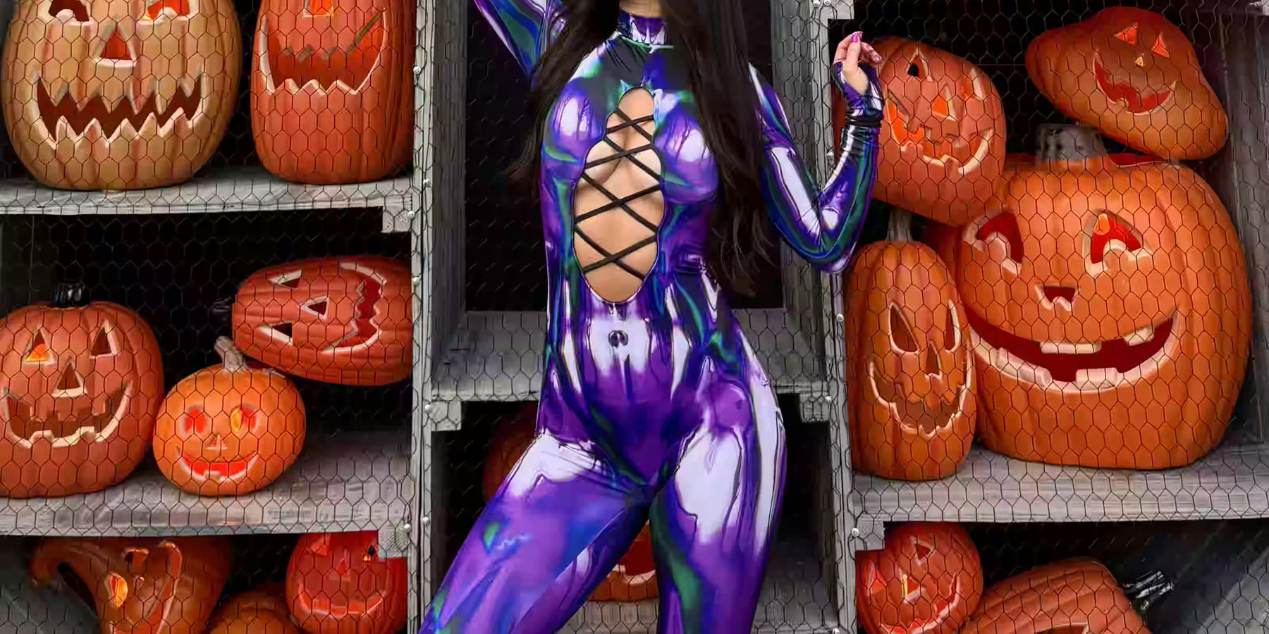 Woman wearing a purple and green long-sleeve cut-out Halloween catsuit, posing in front of carved jack-o'-lanterns, a bold rave outfit idea for BOO Seattle.