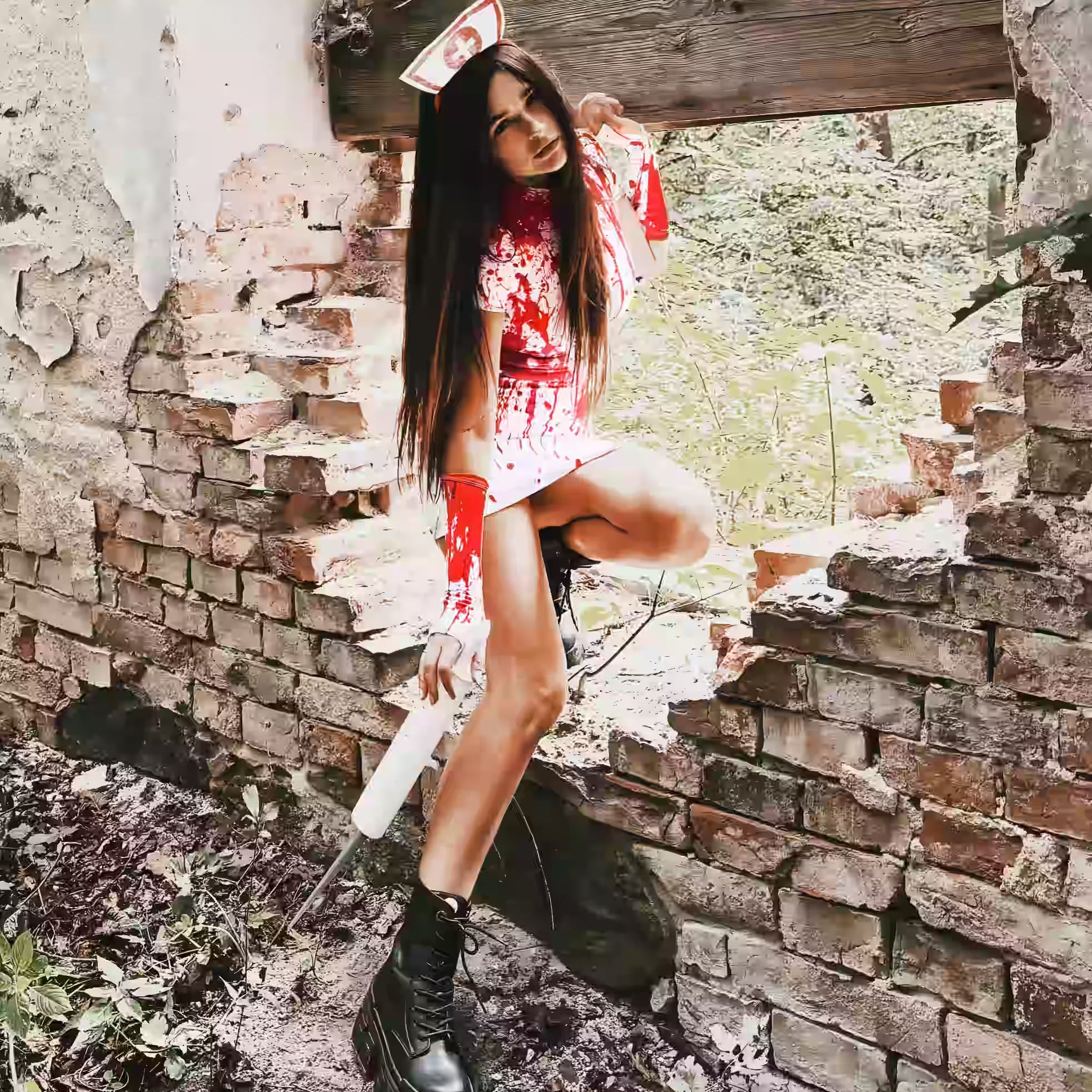 Woman wearing a blood-splattered nurse costume with a matching headpiece and black platform boots, posing in an abandoned brick building.