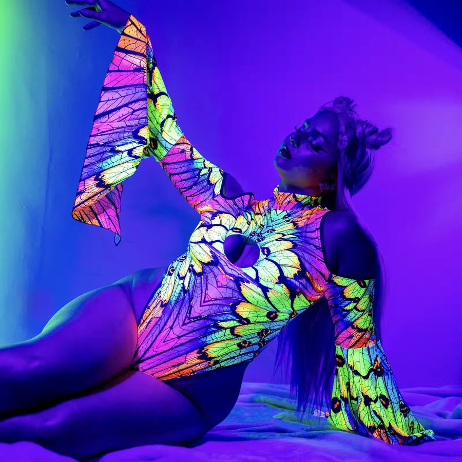Woman wearing a UV-reactive neon butterfly print cut-out bodysuit with flared sleeves, glowing under purple blacklight, a rave outfit idea for MÁS EDM Denver.
