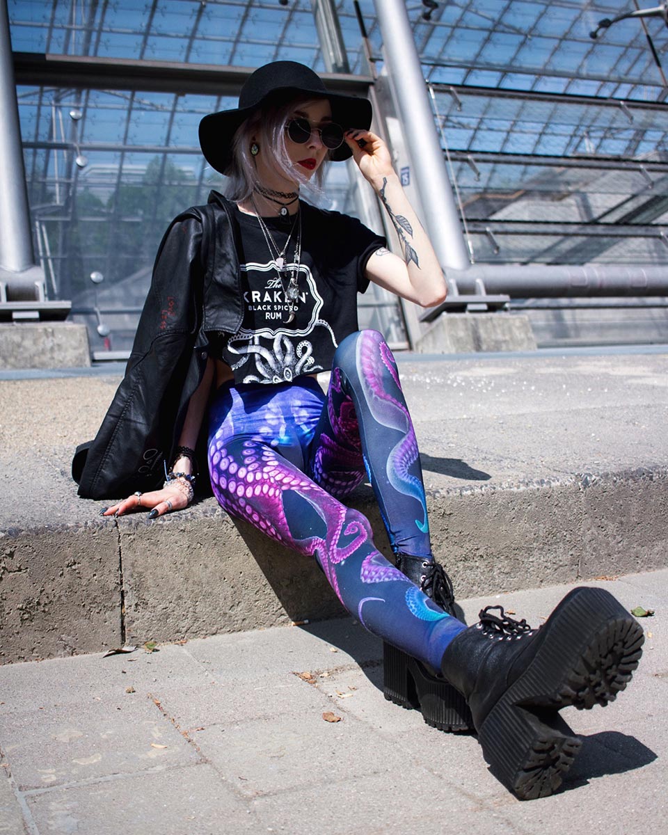 Woman wearing printed octopus leggings and black hat, boots and jacket.